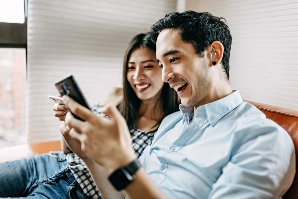 A young couple, including a man with a hearing aid, using their mobile devices.