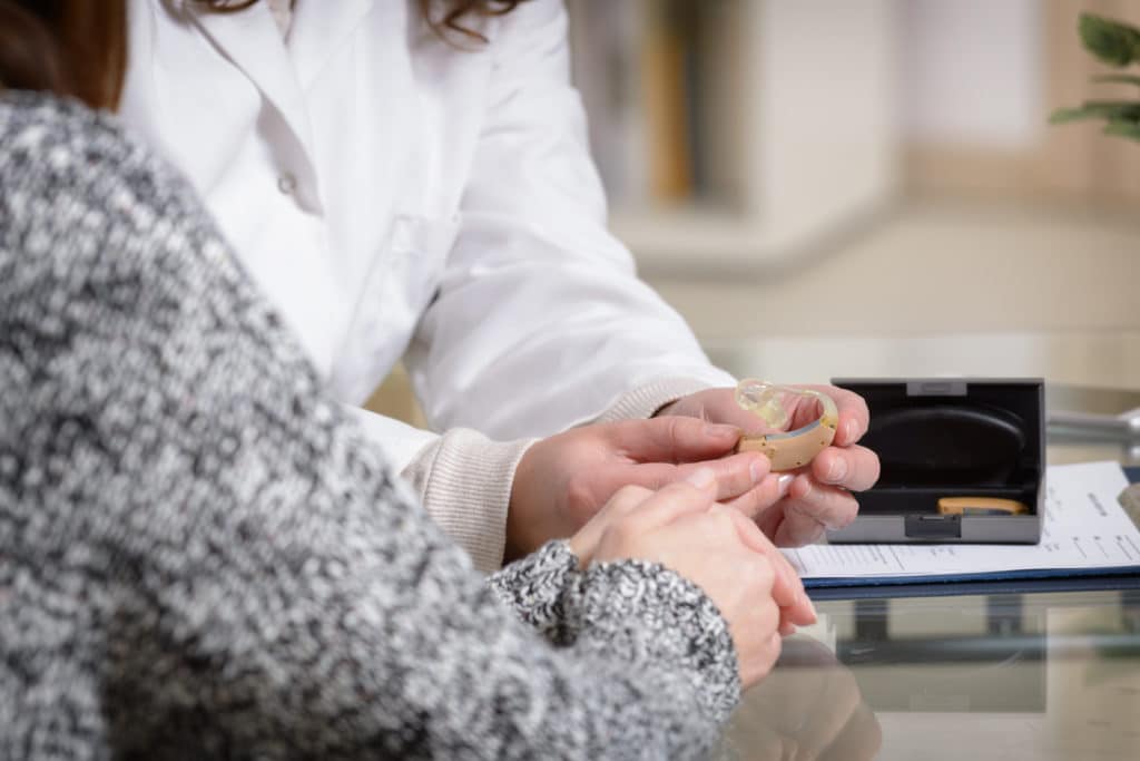 Shows an audiologist and a patient holding a hearing aid Doctor showing hearing aid to her patient in the doctor's office